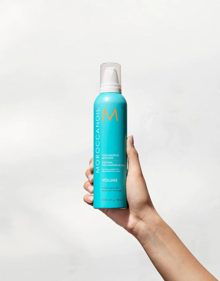 Moroccanoil Volumizing Mousse image of model holding up 8.5 oz bottle