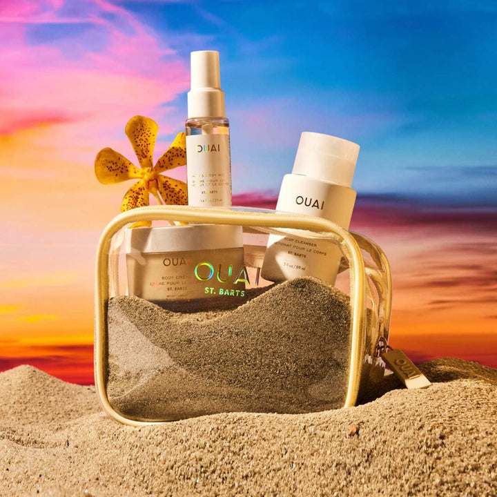 OUAI hair care products in a beach setting with a colorful sky.